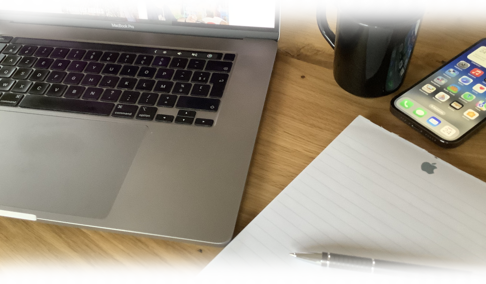 Mac et iPhone posés sur un bureau avec tasse de café, carnet de prise de note et stylo juste à coté